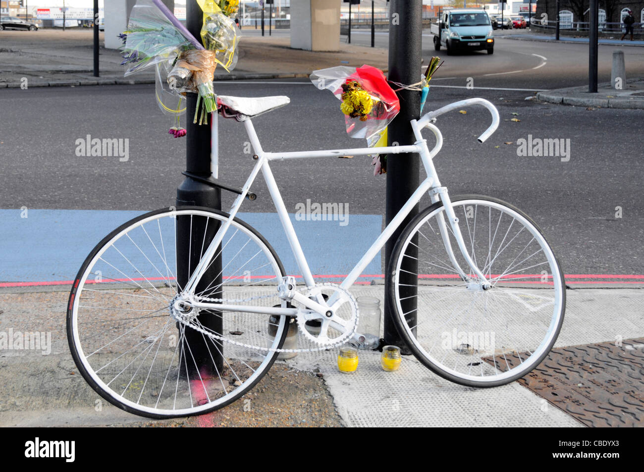 Vélo de couleur blanche memorial et fleurs pour cycliste tué à la jonction de route comprend blue voie cyclable marquage routier Banque D'Images