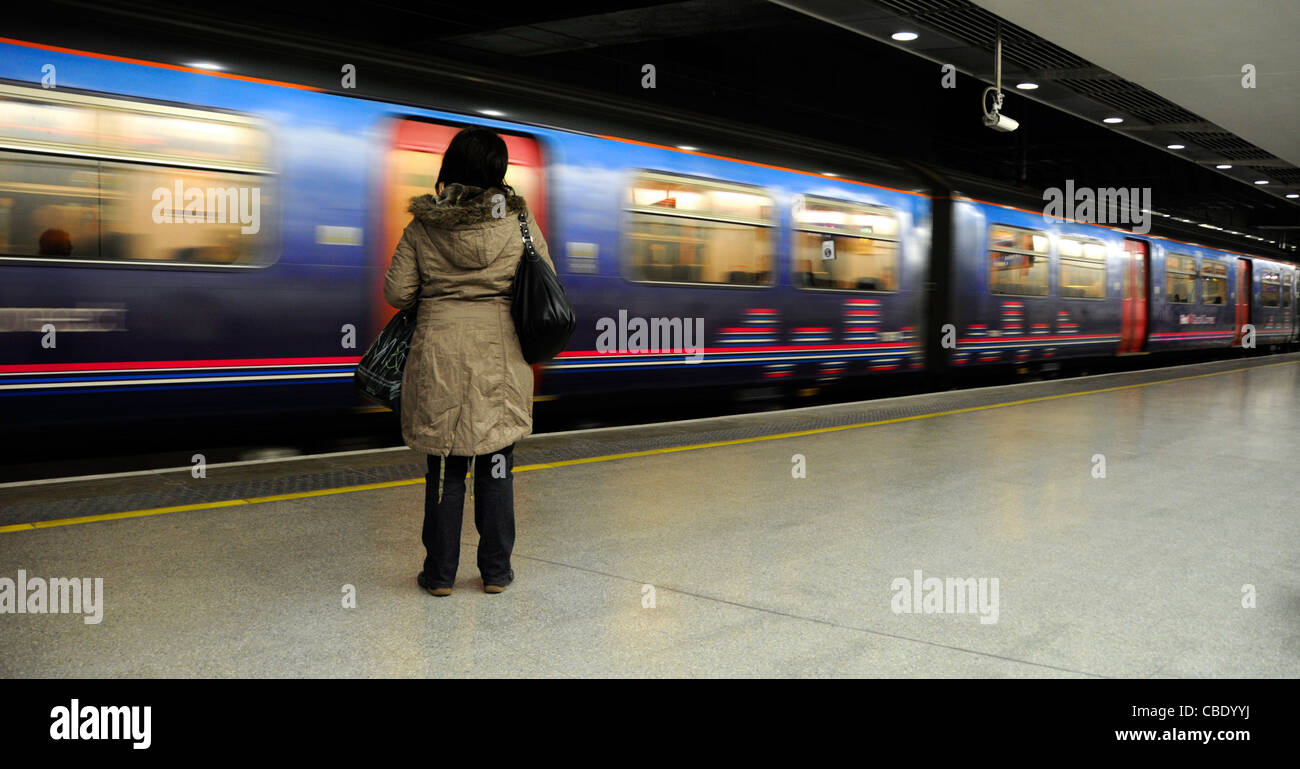 Vue arrière femme seule passager debout seul sur la plate-forme de la gare en mouvement train Thameslink au départ de la gare de St Pancras (niveau bas) Londres Angleterre Royaume-Uni Banque D'Images