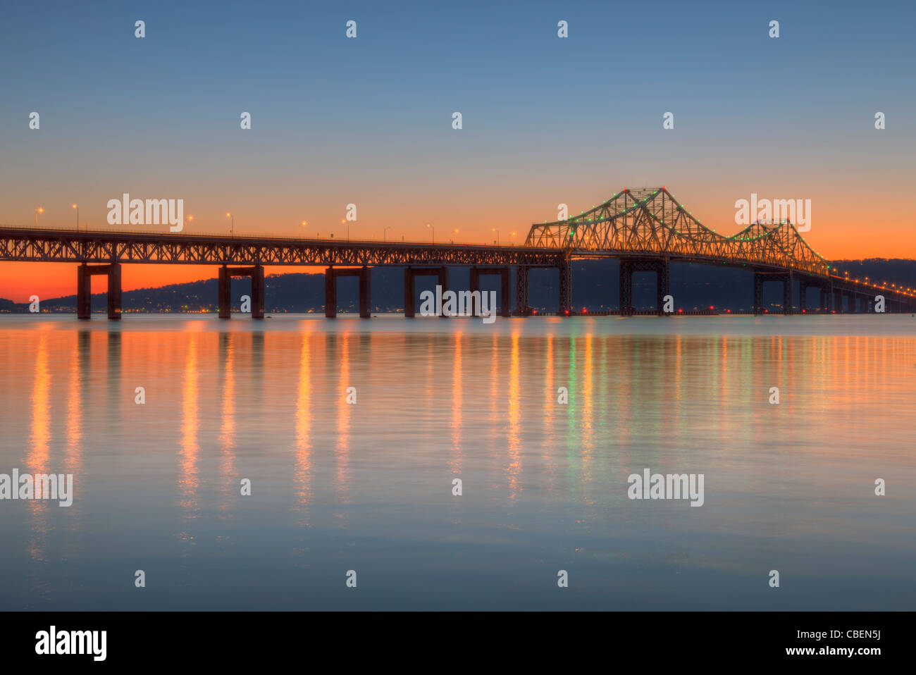 Le ciel de l'ouest est orange après le coucher du soleil derrière le pont Tappan Zee, dont les lumières reflètent sur la surface de la rivière Hudson. Banque D'Images