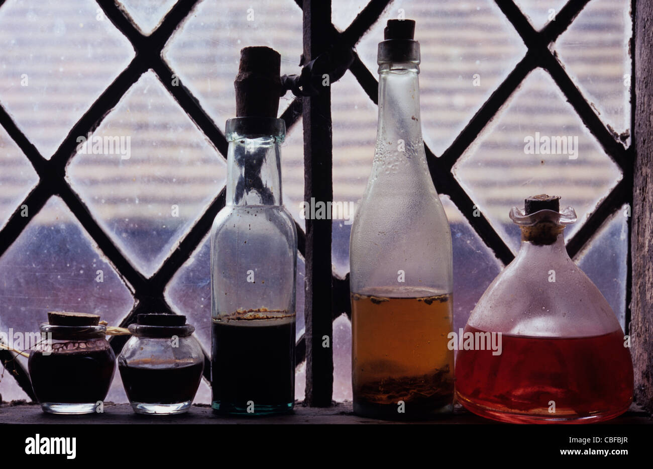 Collection de meubles anciens pots et bouteilles contenant des liquides colorés et debout sur rebord de fenêtre au plomb de diamants Banque D'Images