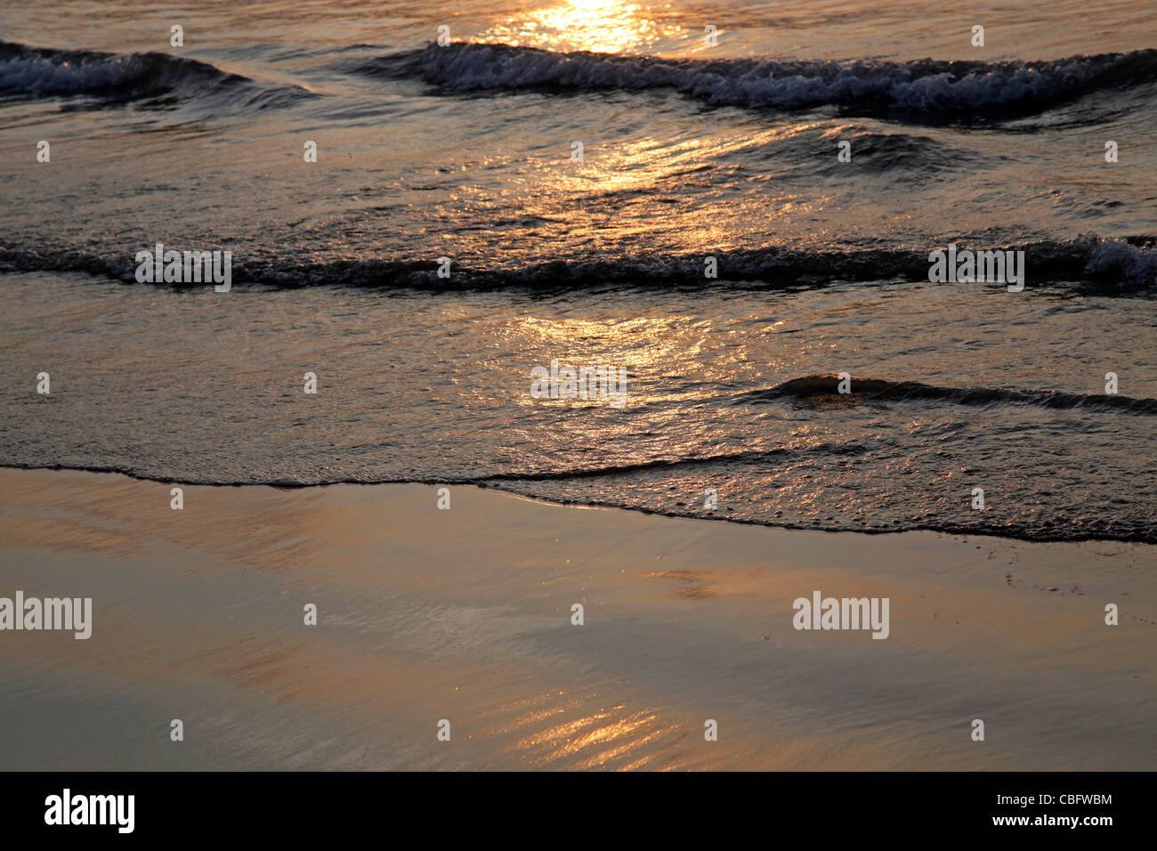 Vagues se brisant sur une paisible plage de sable fin avec la réflexion du soleil sur l'eau de mer au coucher du soleil sur la plage de Patong à Phuket Banque D'Images