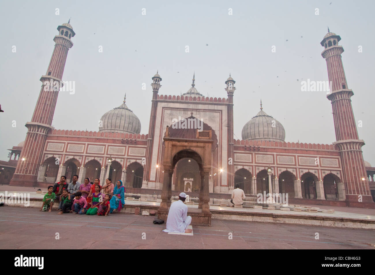 Un homme de méditer, et une famille pose pour la photo en face de la Jama Masjid Banque D'Images