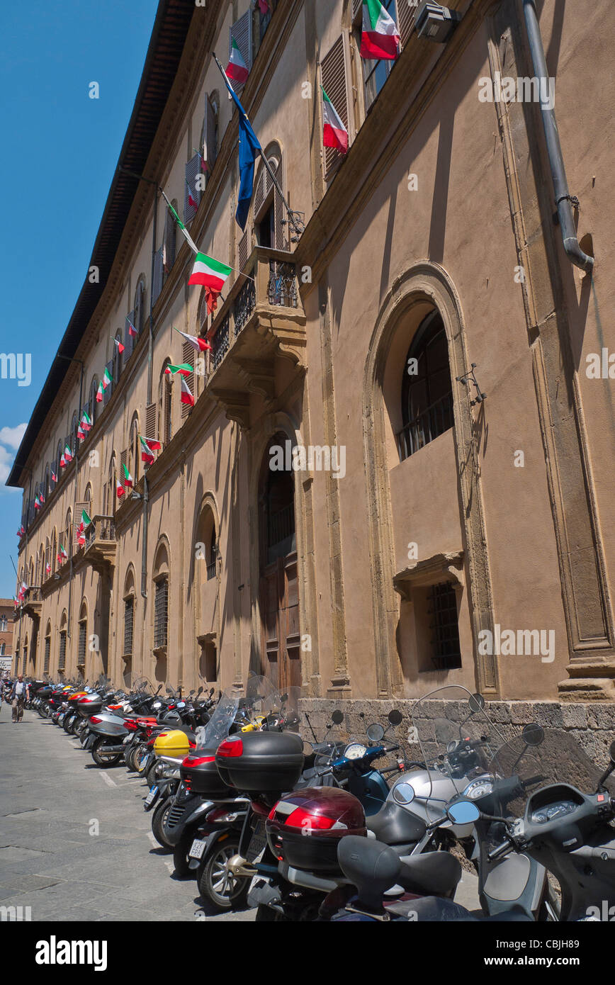 Une rangée d'motorscooters parqué et les motos en ligne le long de la face avant d'un long bâtiment à Sienne, Italie. Banque D'Images
