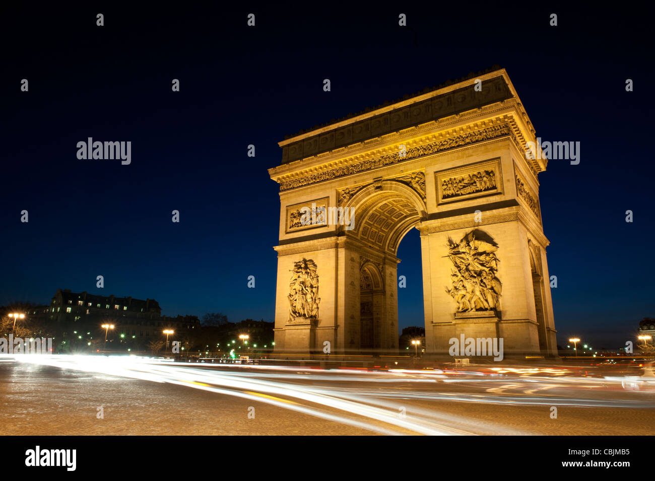 L'Arc de Triomphe depuis le rond-point englobant le soir, avec des sentiers de lumière de la circulation. Banque D'Images
