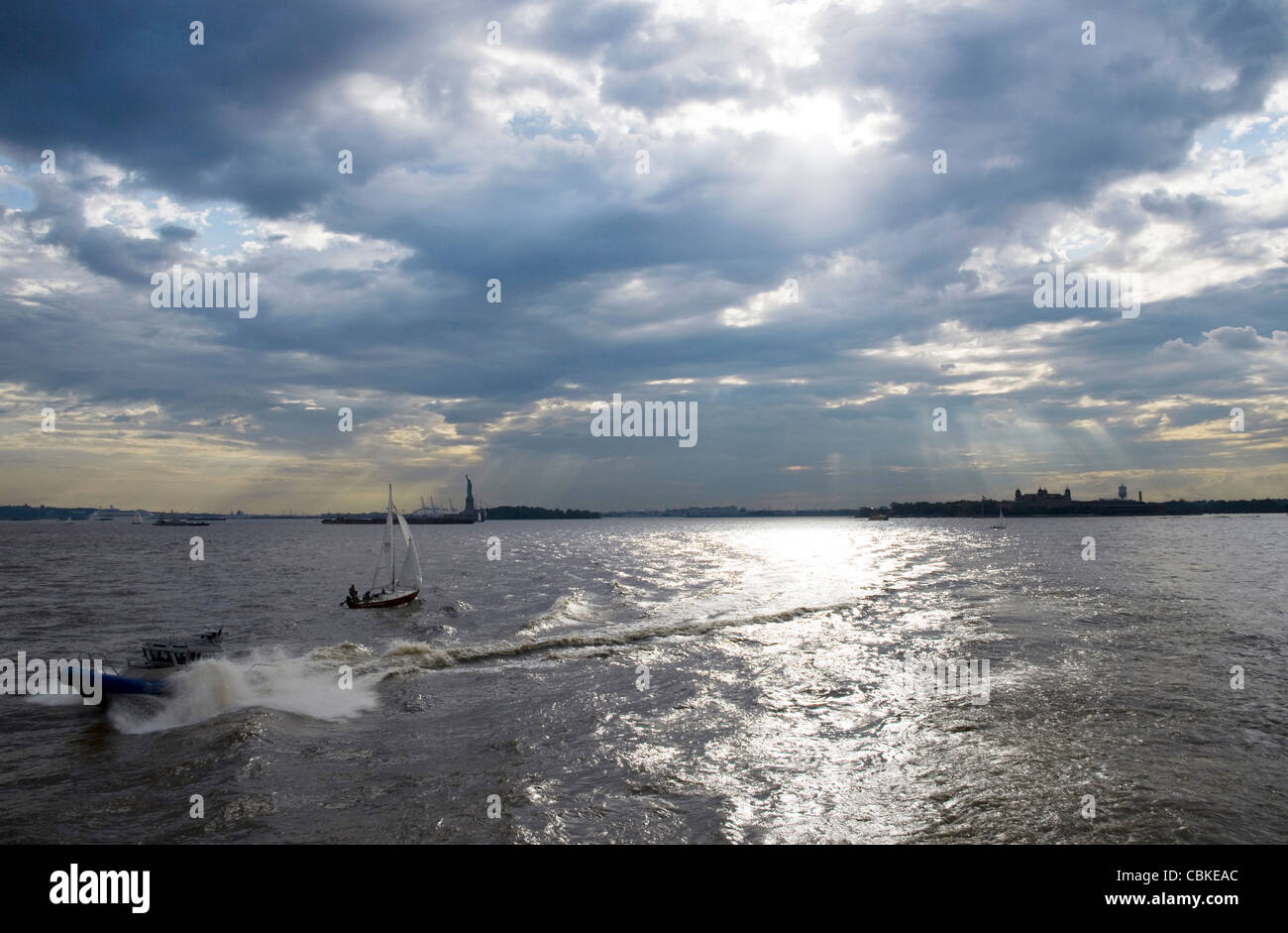 Le port de New York en fin d'après-midi sous un ciel couvert avec Statue de la Liberté et Ellis Island qui se profile au loin. Banque D'Images