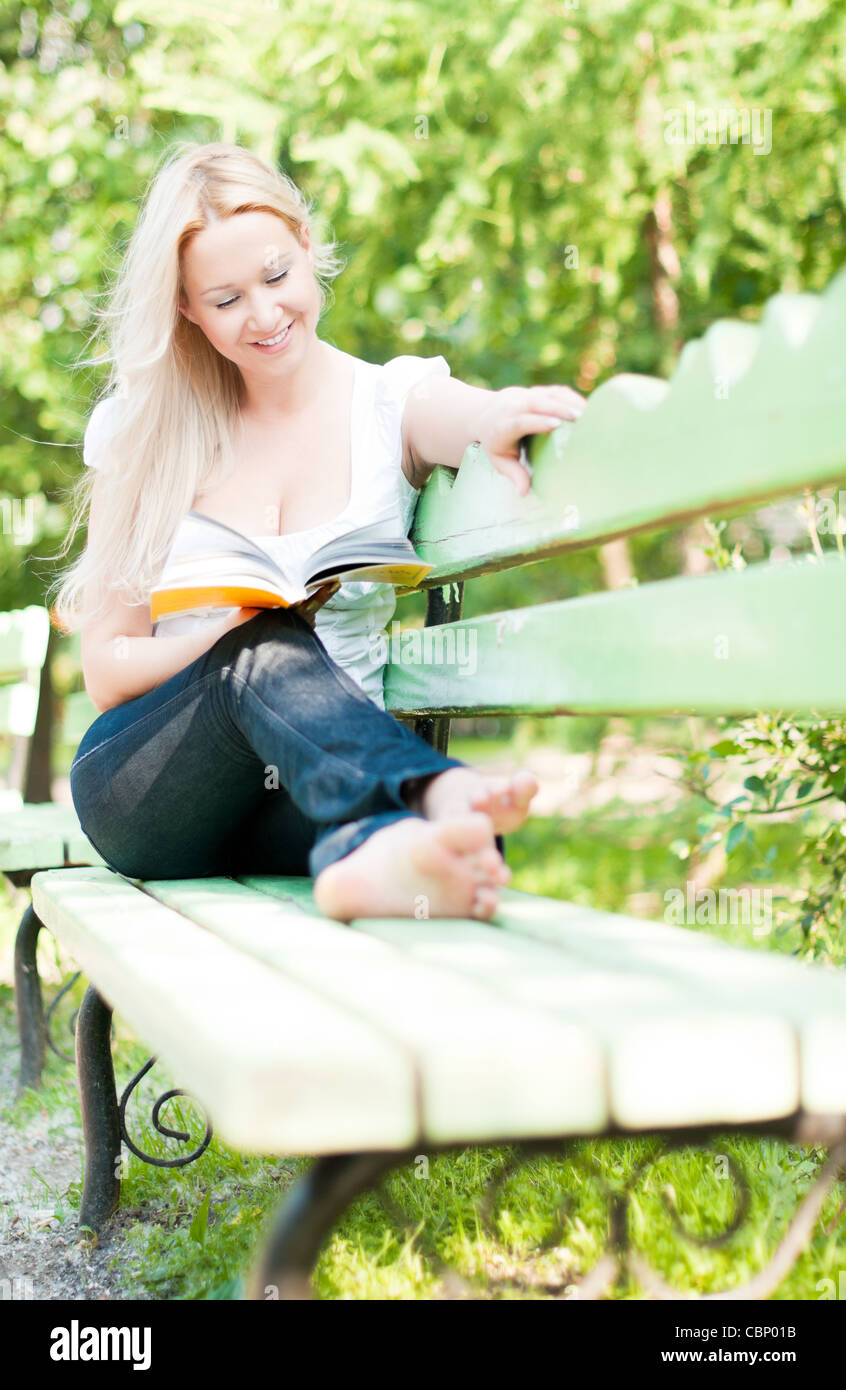 Jeune femme assise sur un banc dans le parc, reading book and smiling Banque D'Images