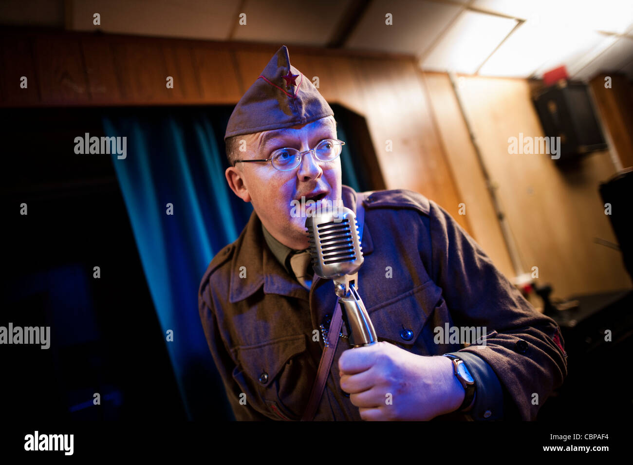 Un compere MC vêtu comme un soldat GI parlant parlant dans un micro à un retro 40s 50s music club, UK Banque D'Images