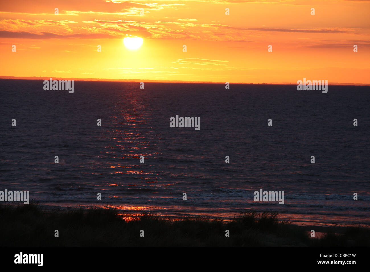 Coucher du Soleil reflété sur mer, or et orange glow ciel nocturne Banque D'Images