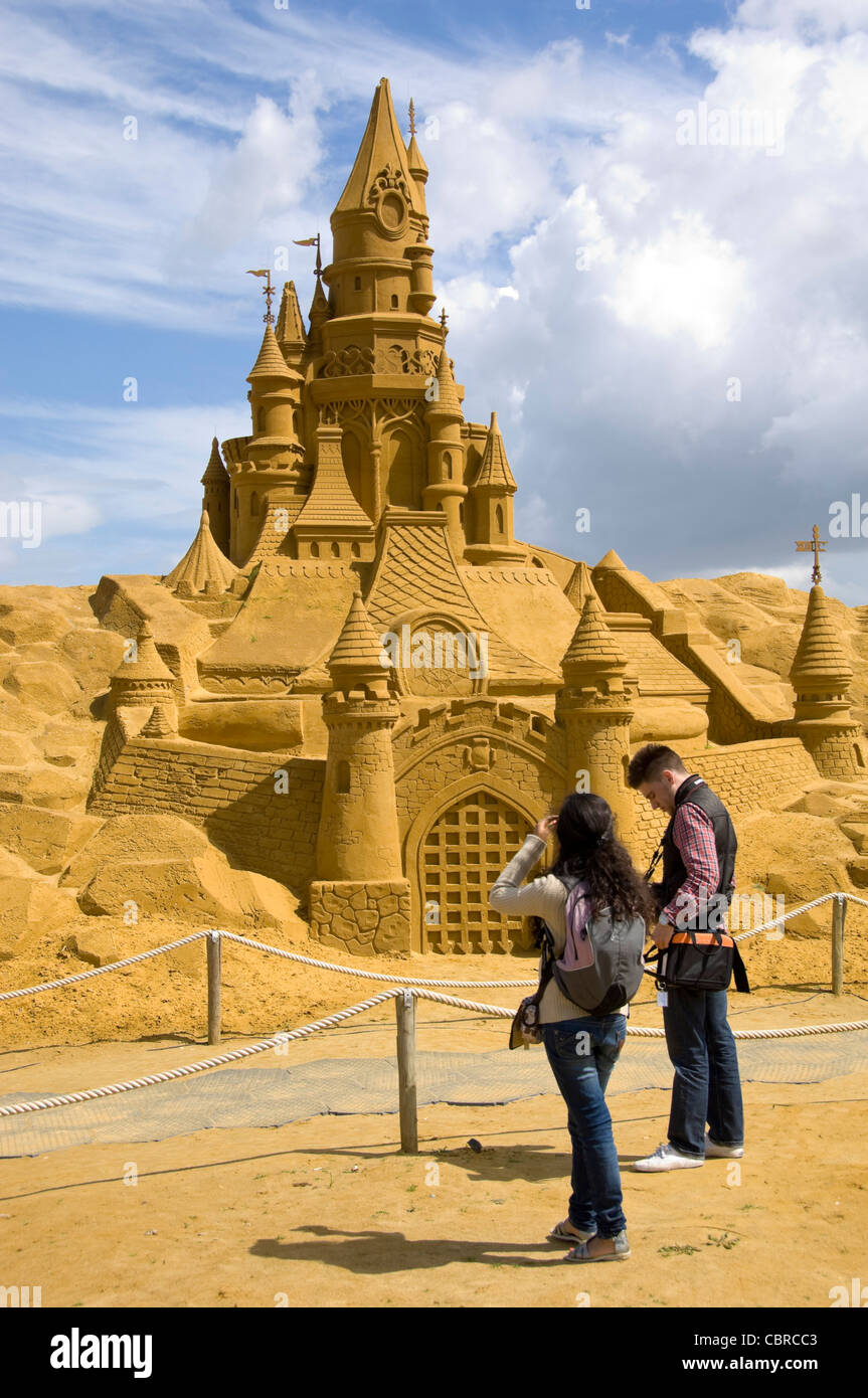 Close up vertical d'une incroyable sculpture de sable d'un immense château avec des gens debout en face de lui donner l'échelle, on a sunny day Banque D'Images