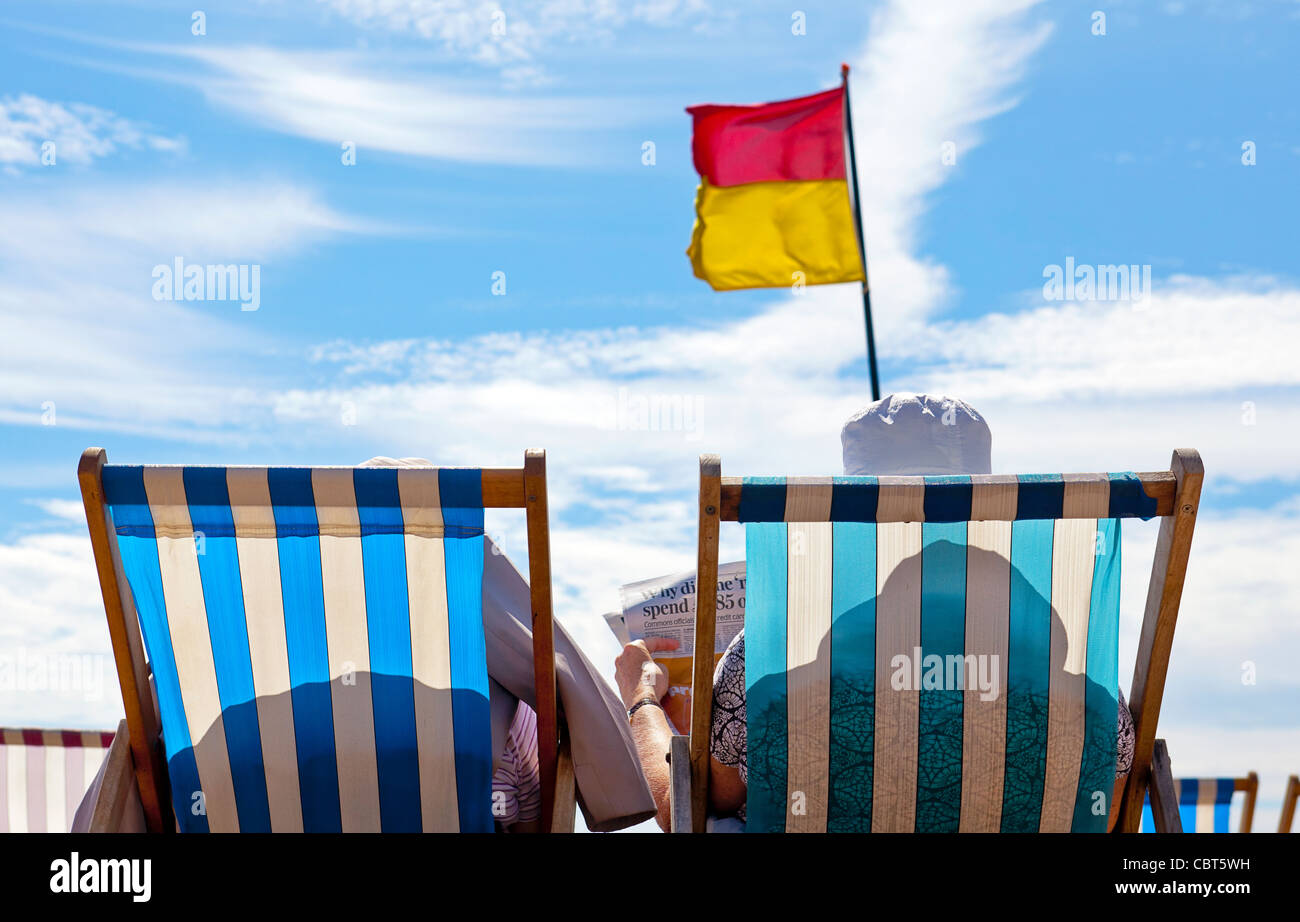 Deux femmes âgées et à la retraite sont assises dans des chaises de plage pour se détendre sur la plage de l'océan. Banque D'Images