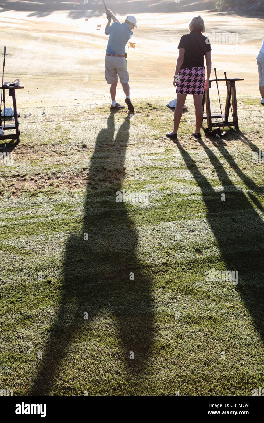 Une femme observe un golf pro golfeur mâle hits une balle sur la gamme de conduite en début de matinée avec de longues ombres à l'Abama reso Banque D'Images