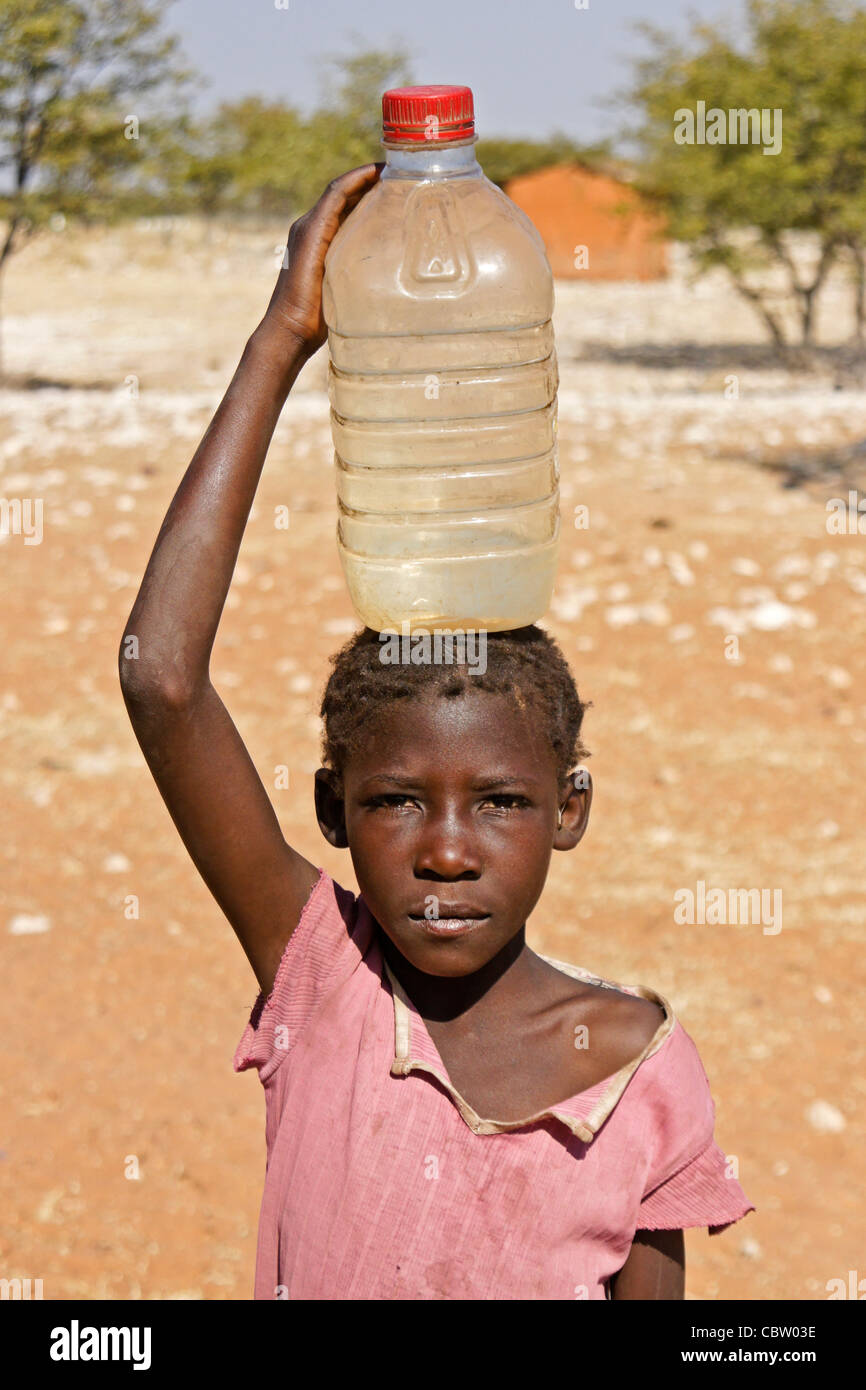 Fille Herero portant de l'eau dans le village, le Damaraland, Namibie Banque D'Images