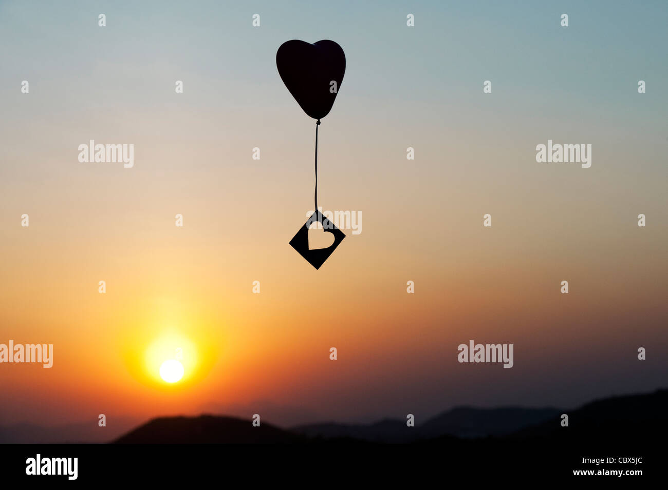 Avec ballon coeur découper des forme de coeur à la dérive dans un ciel de coucher du soleil. Silhouette Banque D'Images