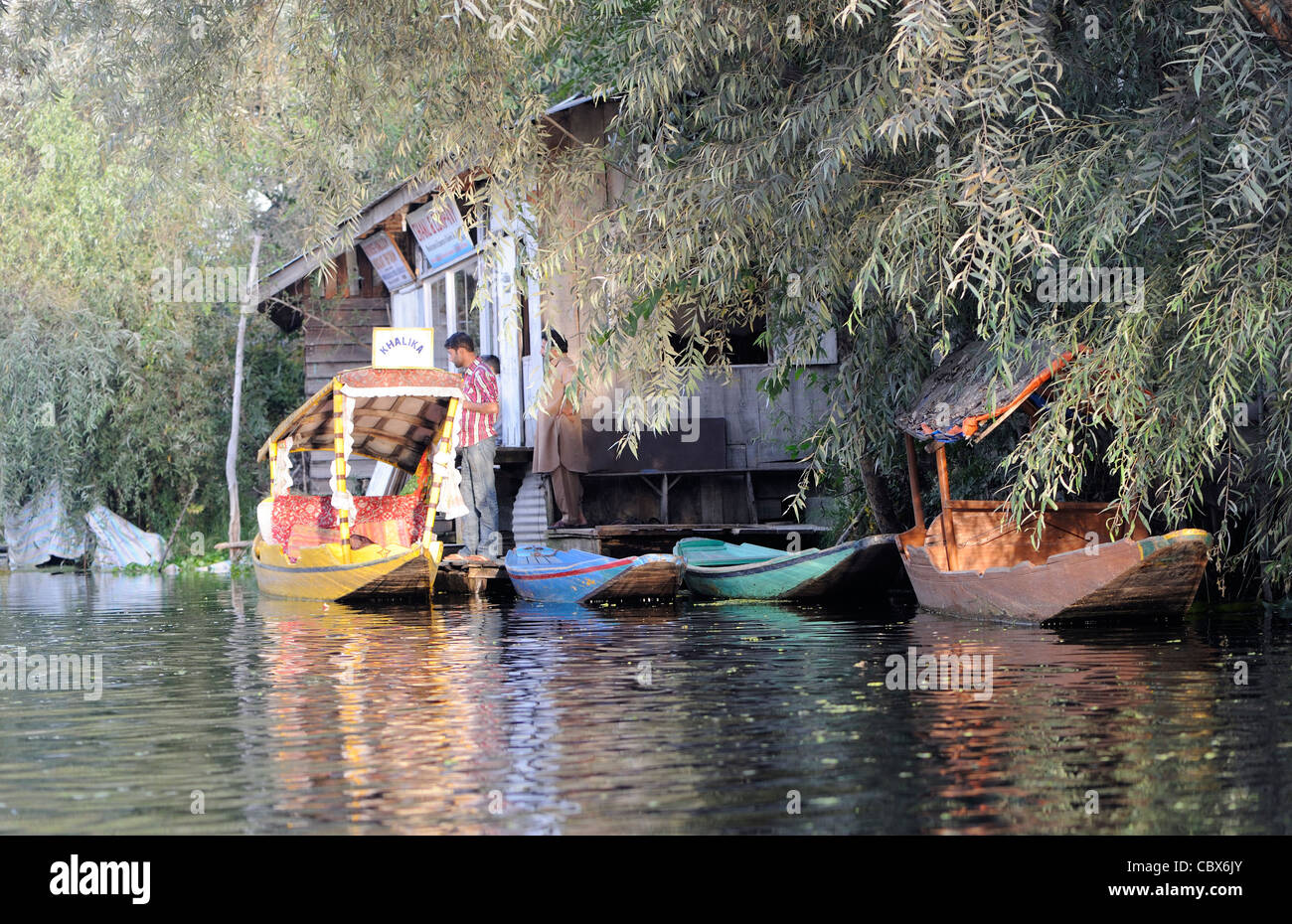 Un shikara, petit bateau taxi de l'eau en bois, et d'autres petits bateaux amarrés par un atelier sur le lac Dal. Le lac Dal à Srinagar, au Cachemire. Banque D'Images