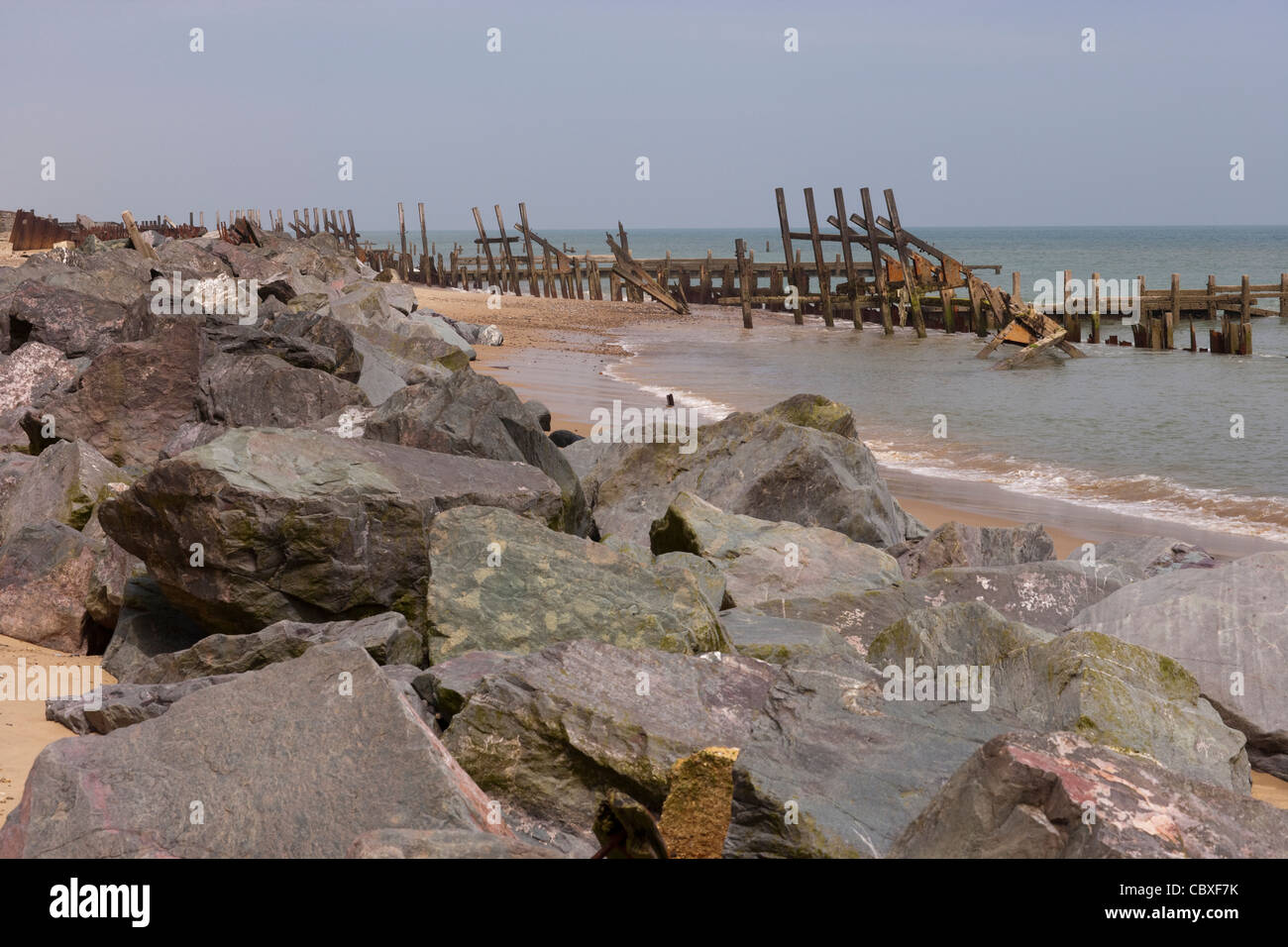 Happisburgh beach, North Norfolk. Bois cassé et brakewaters les roches de granit importés placés réduisent la résistance des marées entrant Banque D'Images
