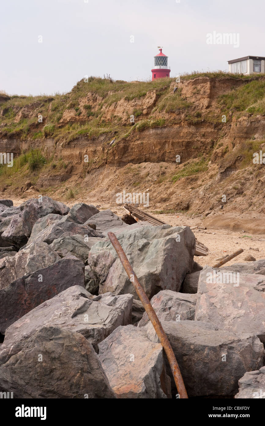 Happisburgh Phare à plus de falaises érodées. Les roches de granit importés placés au premier plan pour améliorer la puissance de la marée montante Banque D'Images