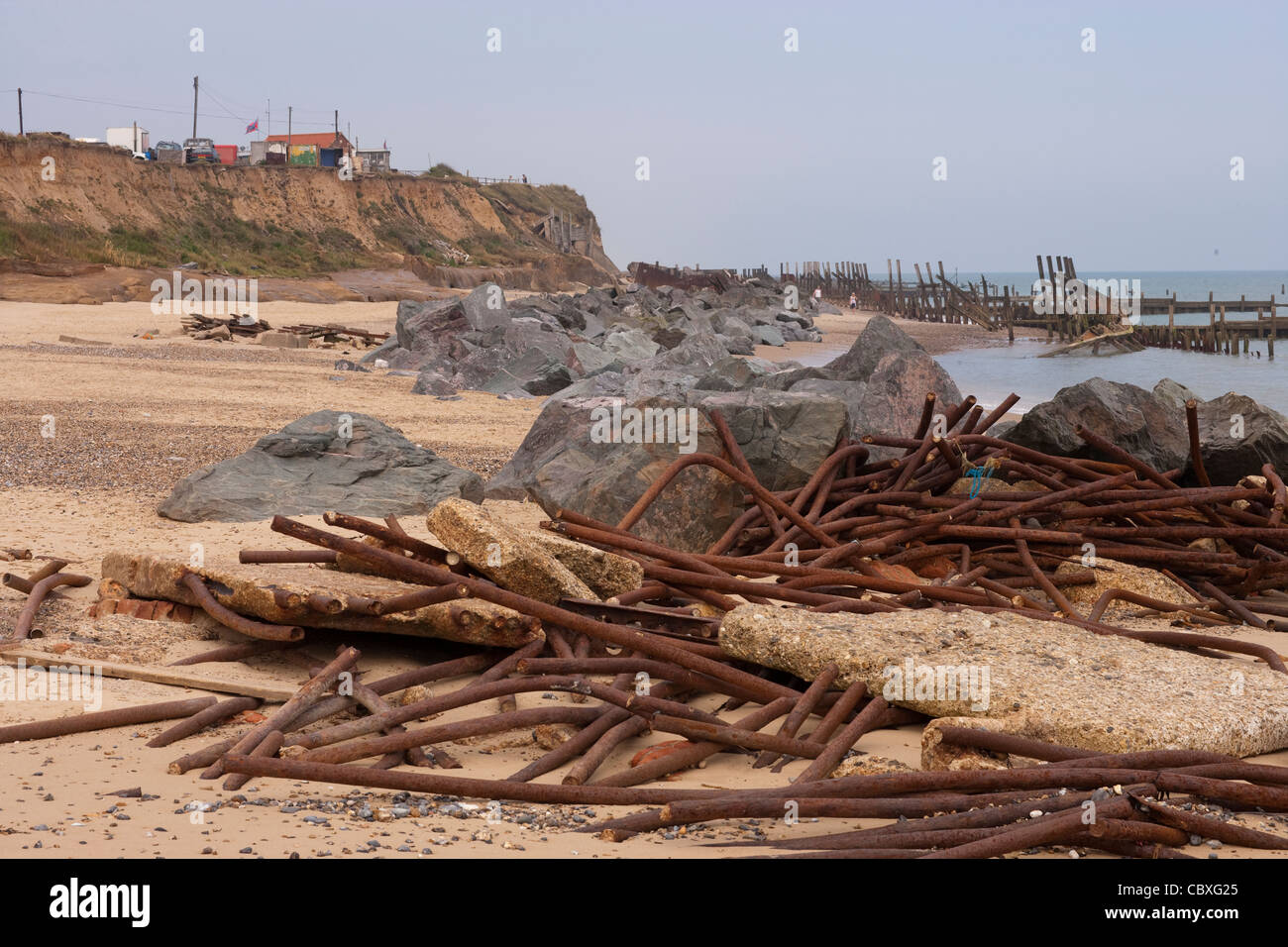 Happisburgh littoral avec la mer accumulée détruit les défenses de métal dans les roches de granit importés pile derrière, détruit les disjoncteurs de bois plus loin encore. Banque D'Images