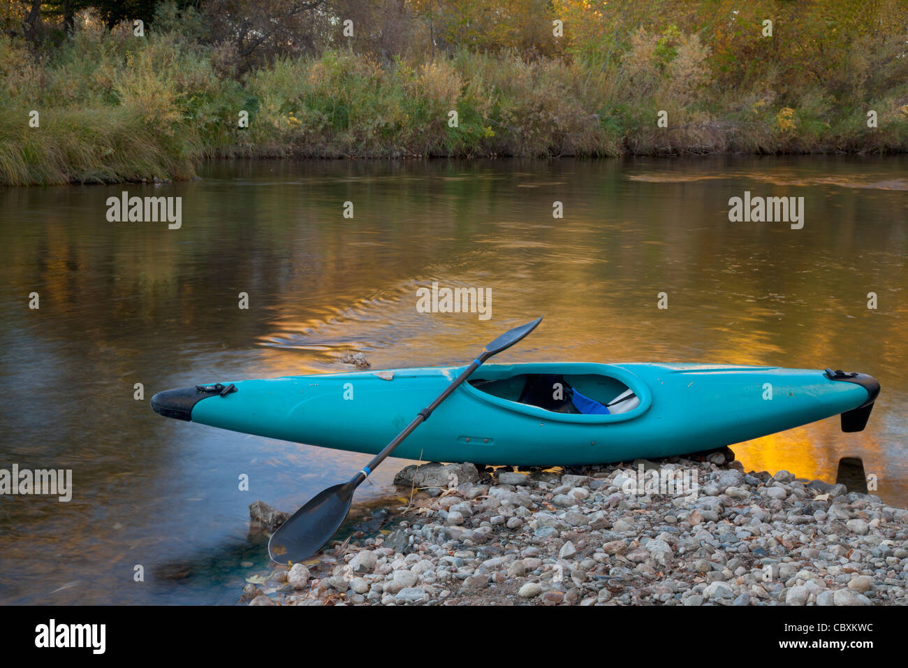 Kayak bleu sur un rivage rocailleux contre river avec réflexion couleur or Banque D'Images