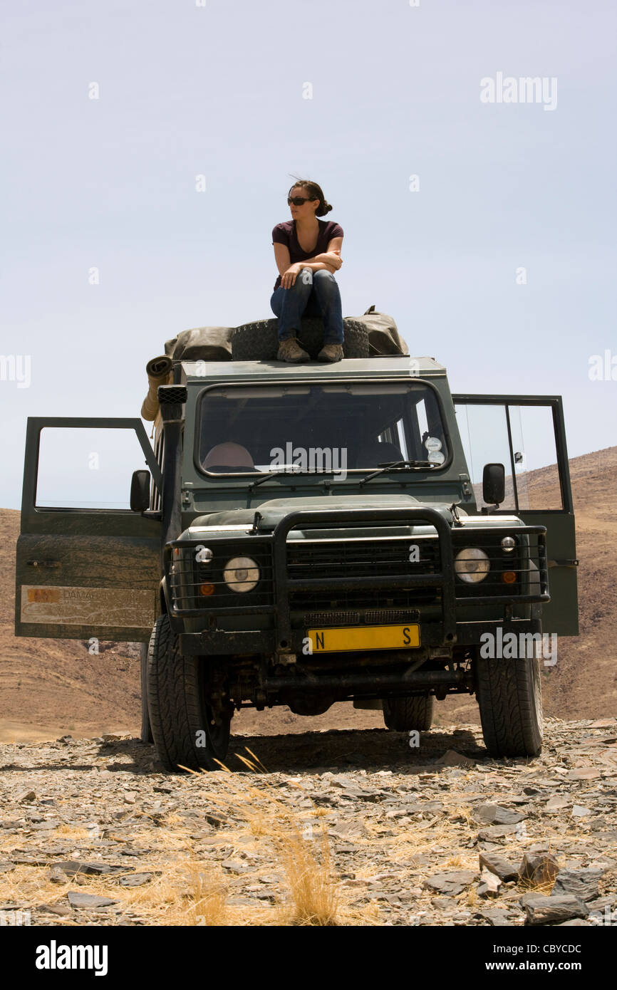 Jeune femme assise sur le dessus de véhicule safari - Purros Conservancy - Kaokoland, région de Kunene, Namibie, Afrique Banque D'Images