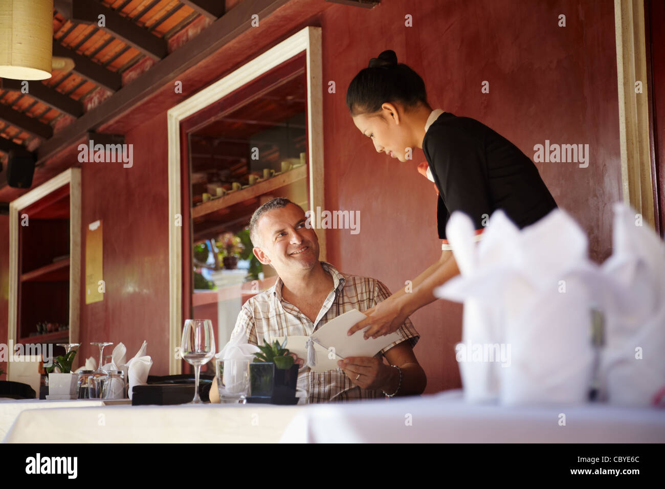 Young Asian woman travailler comme serveuse dans un restaurant exclusif à la clientèle et à y assister avec menu Banque D'Images