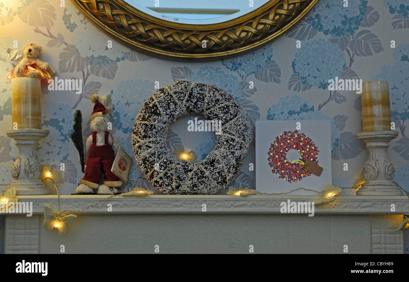 Les lumières de Noël, bougies et divers vide-poches de Noël sur un feu surround avec miroir orné ronde. Banque D'Images