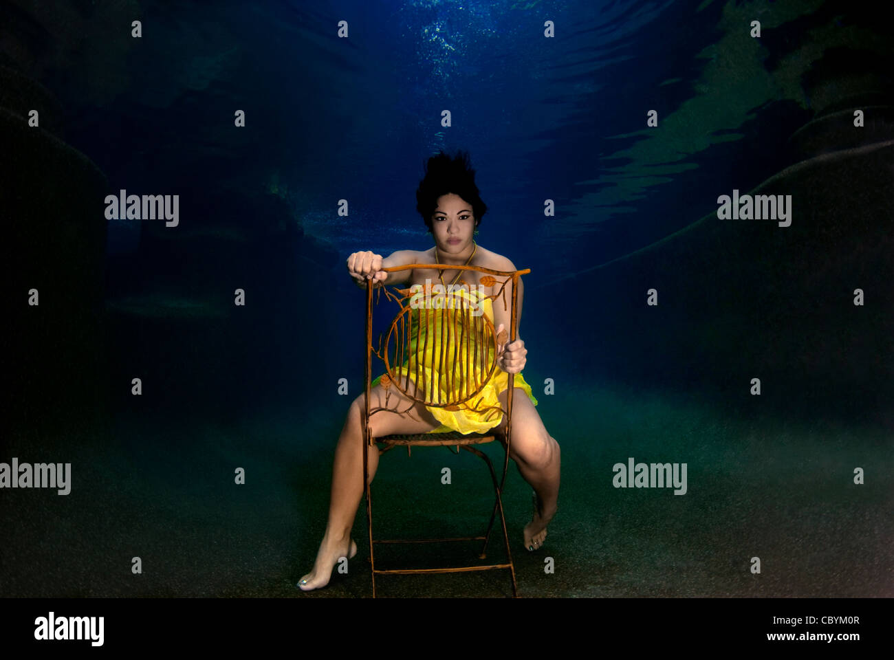 Femme dans une robe jaune assis sur une chaise sous l'eau Banque D'Images