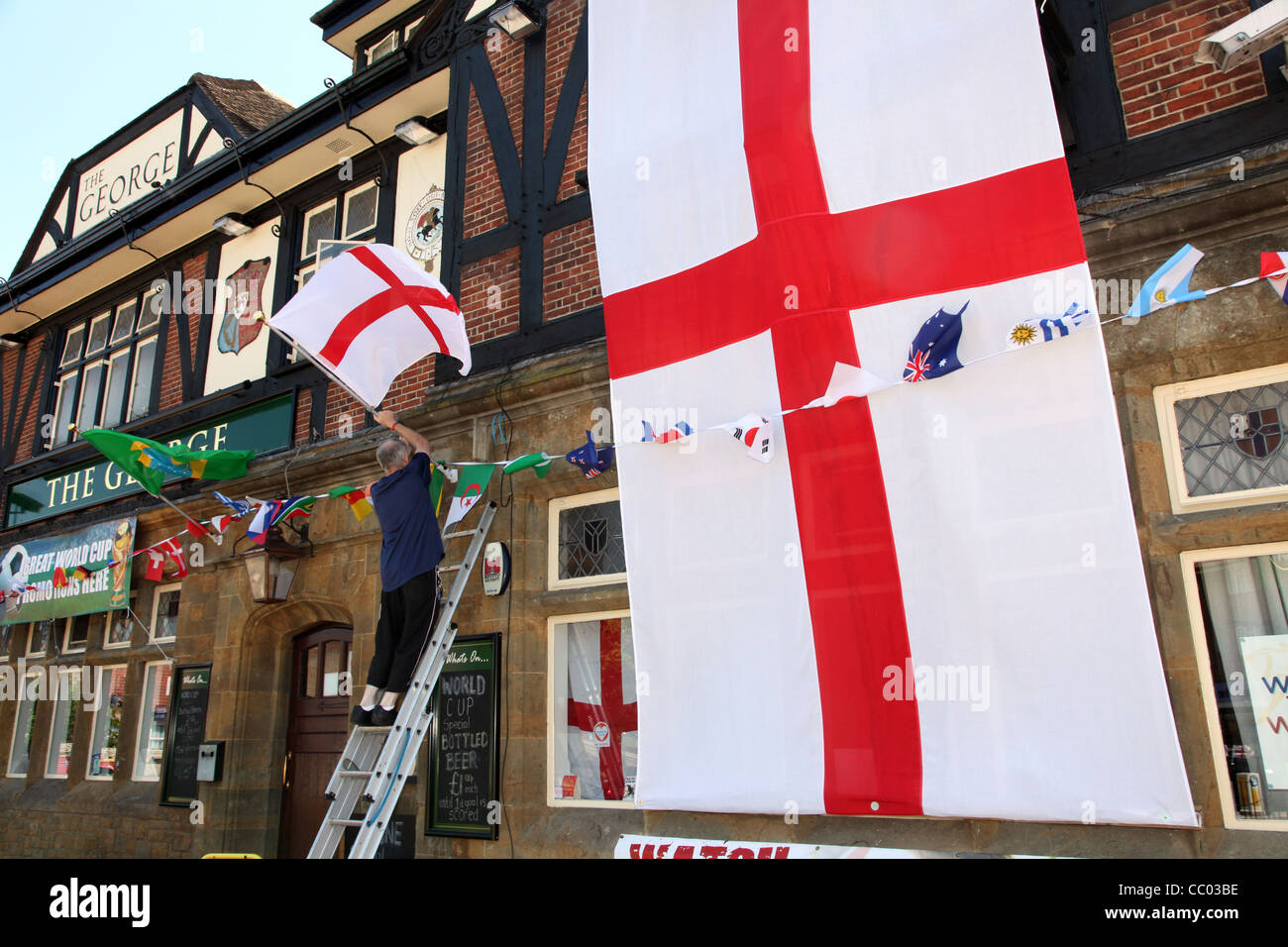 Homme attachant des drapeaux à l'extérieur du pub George dans Kingsbury, Londres Banque D'Images