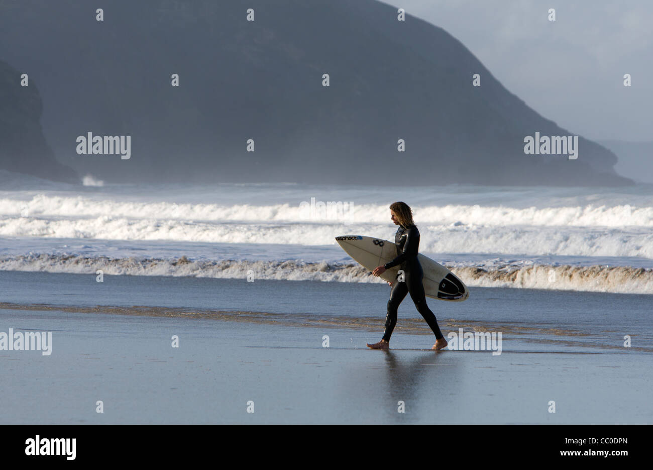 Un surfeur marche de la mer avec sa planche de surf sous le bras à Porthtowan beach, Cornwall Banque D'Images