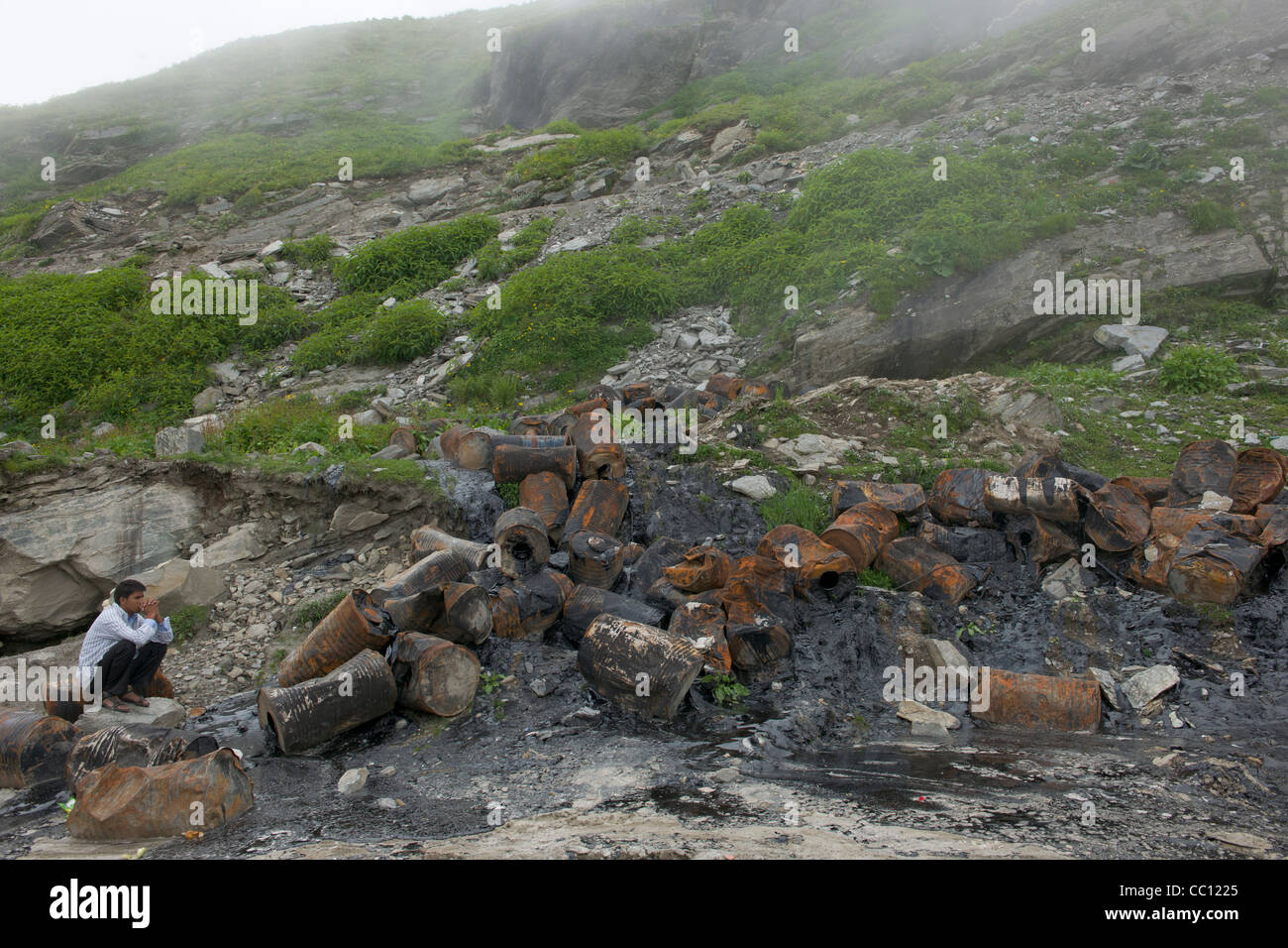 Homme accroupi en fûts de carburant brûlé au Rohtang, sur la route Leh-Manali, Himachal Pradesh, Inde Banque D'Images