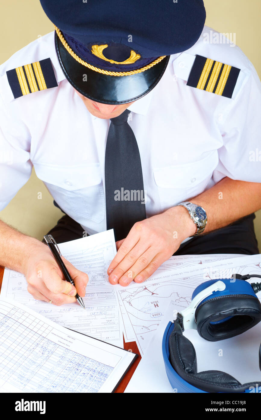 Pilote de ligne souriant wearing hat, chemise avec épaulettes et cravate avec stylo à la main prêt à remplir des papiers et de contrôle p vol Banque D'Images