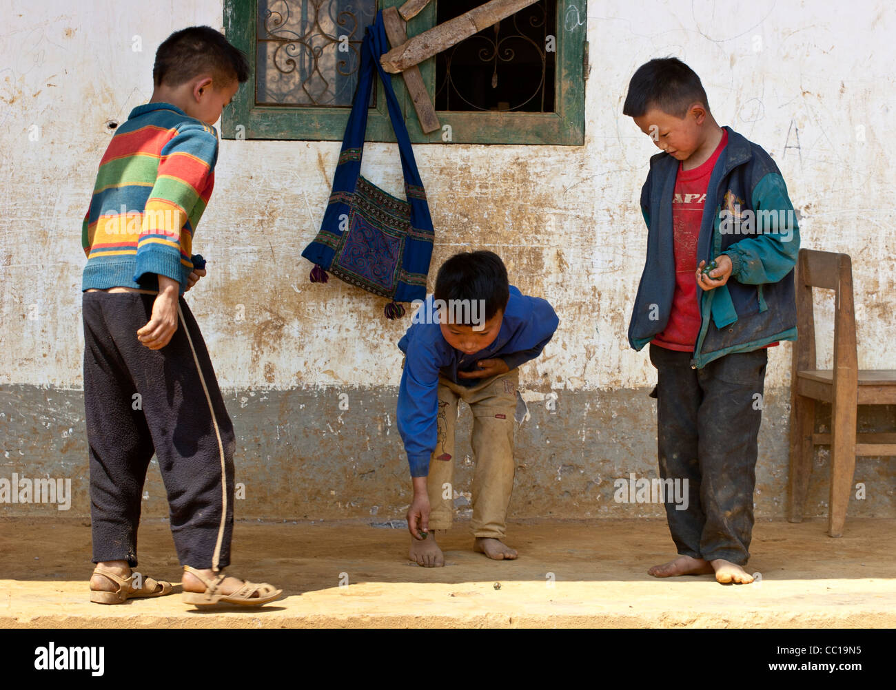 Trois petits garçons dans un village vietnamien de jouer à un jeu (billes) Banque D'Images