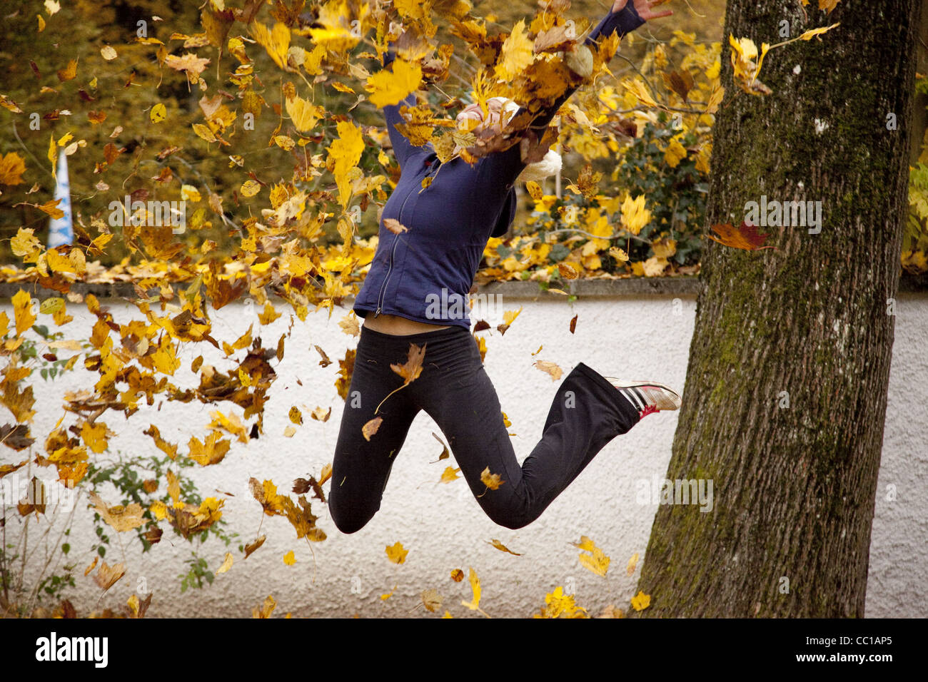 Une fille saute avec les jambes pliées et jette des feuilles jaunes dans l'air sur un après-midi d'automne. Banque D'Images