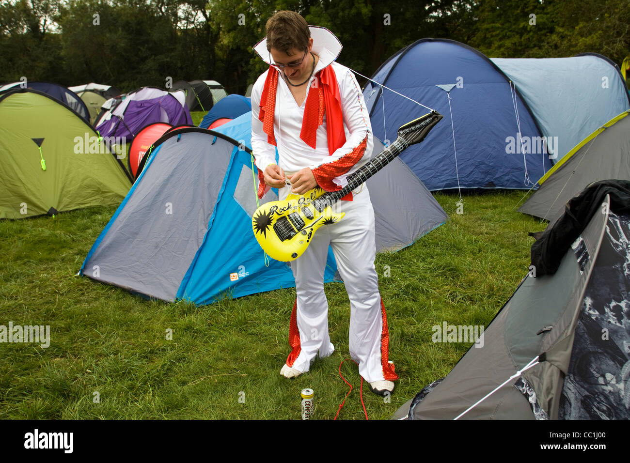 Un homme habillé en Elvis Presley tente de fixer sa guitare gonflable avec de la ficelle à l'extérieur de sa tente au Festival Standon Banque D'Images
