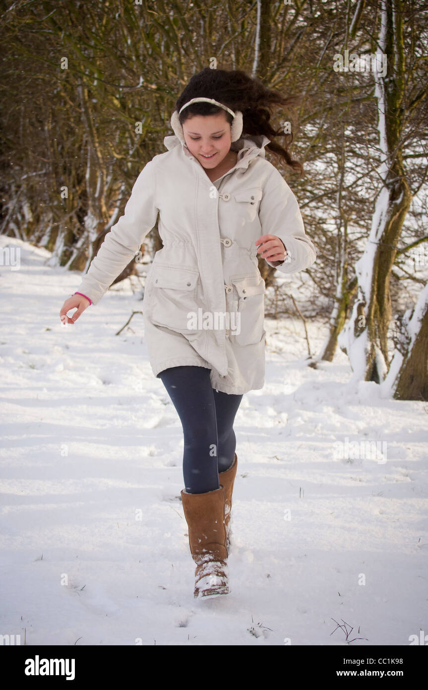 Jeune femme caucasienne en plein air courir dans la neige portant un manteau  blanc chaud, des bottes, des couvre-oreilles Photo Stock - Alamy