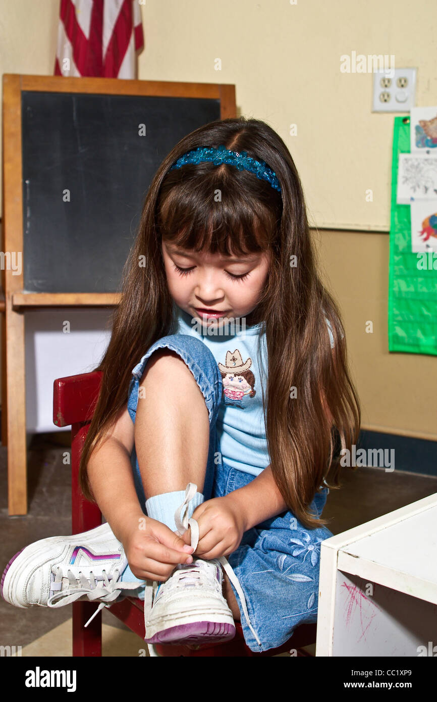 L'Interracial entre 4-5 ans ans raciale girl learning pour attacher ses chaussures en sroom clas. M. © Myrleen Pearson Banque D'Images
