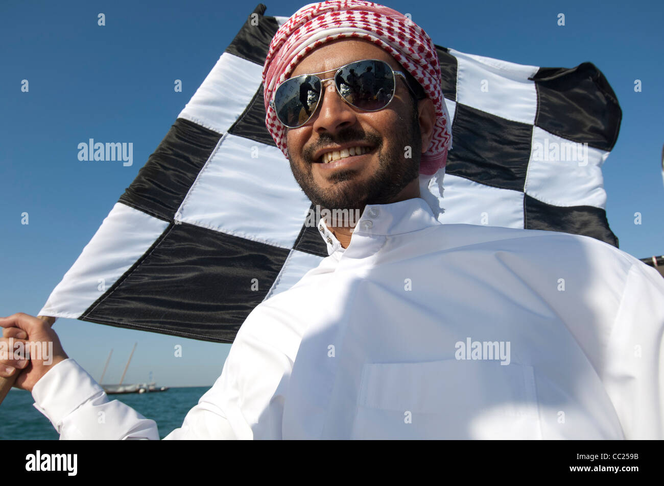 Un émirat man wearing sunglasses vagues un drapeau à damier en mer, Dubaï Banque D'Images