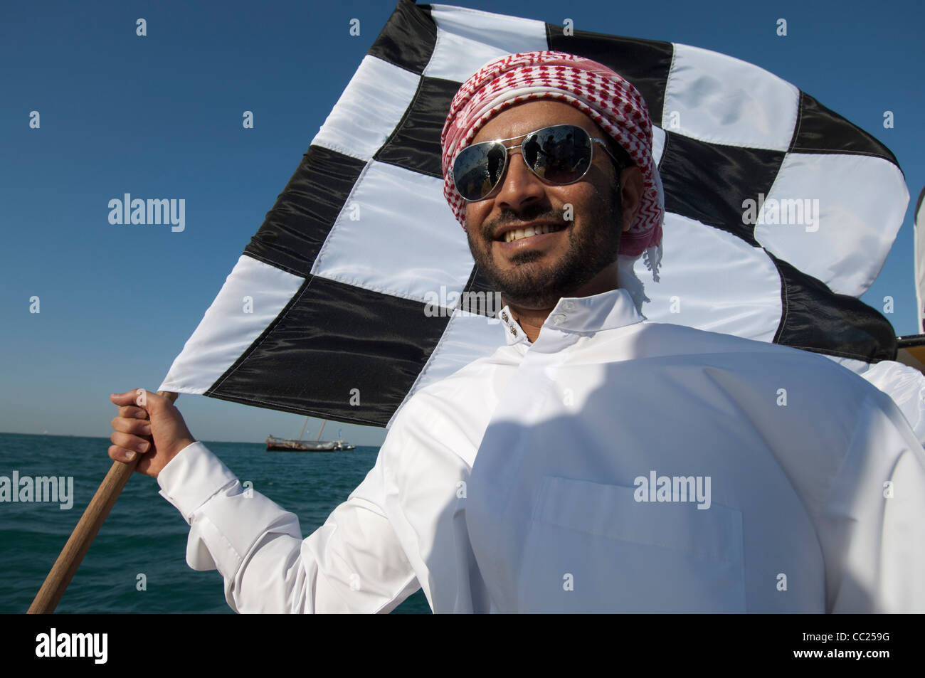 Un émirat man wearing sunglasses vagues un drapeau à damier en mer, Dubaï Banque D'Images