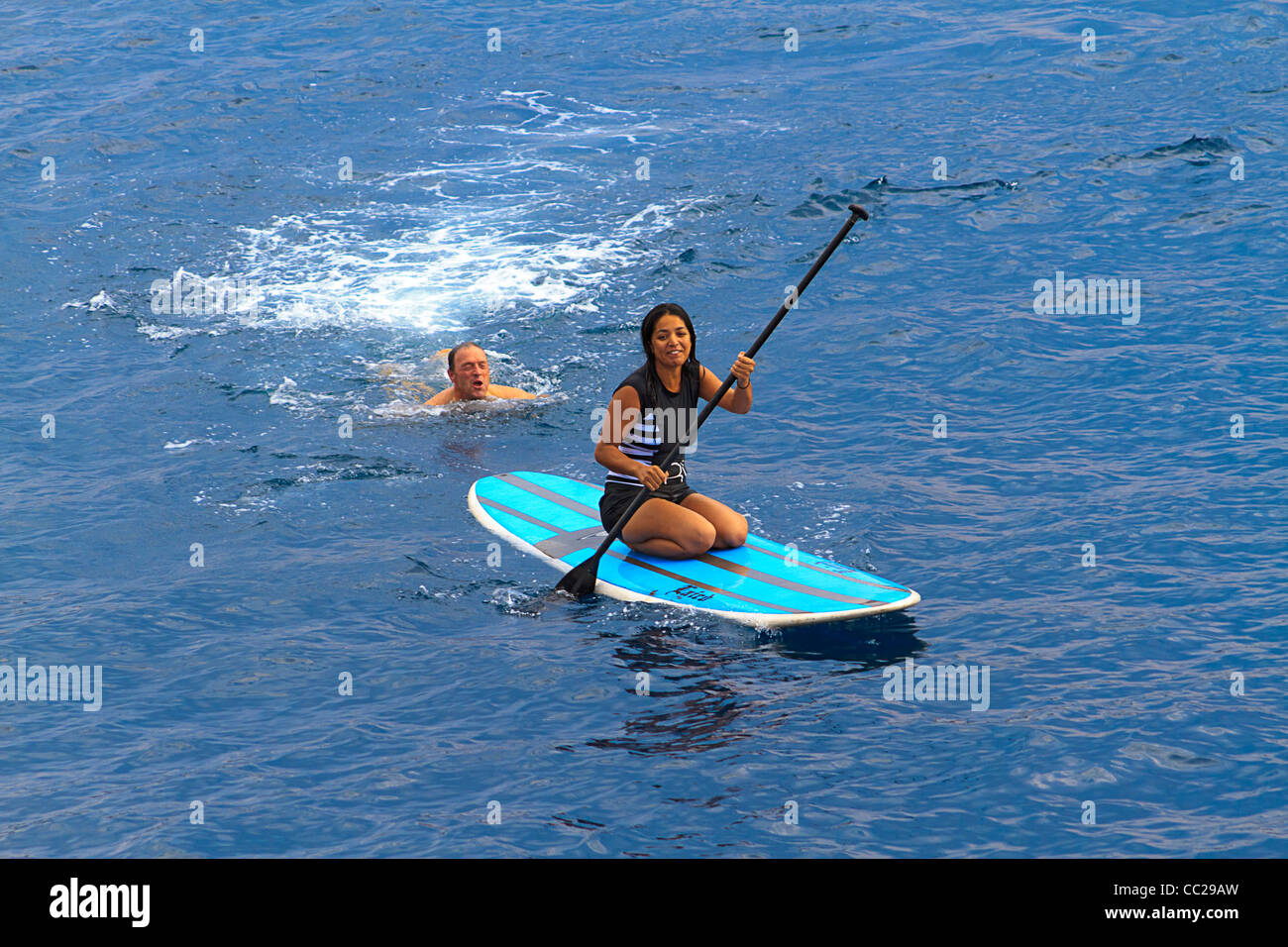 Standup paddleboard sur femme tandis que l'homme nage derrière elle à Hawaï. Banque D'Images