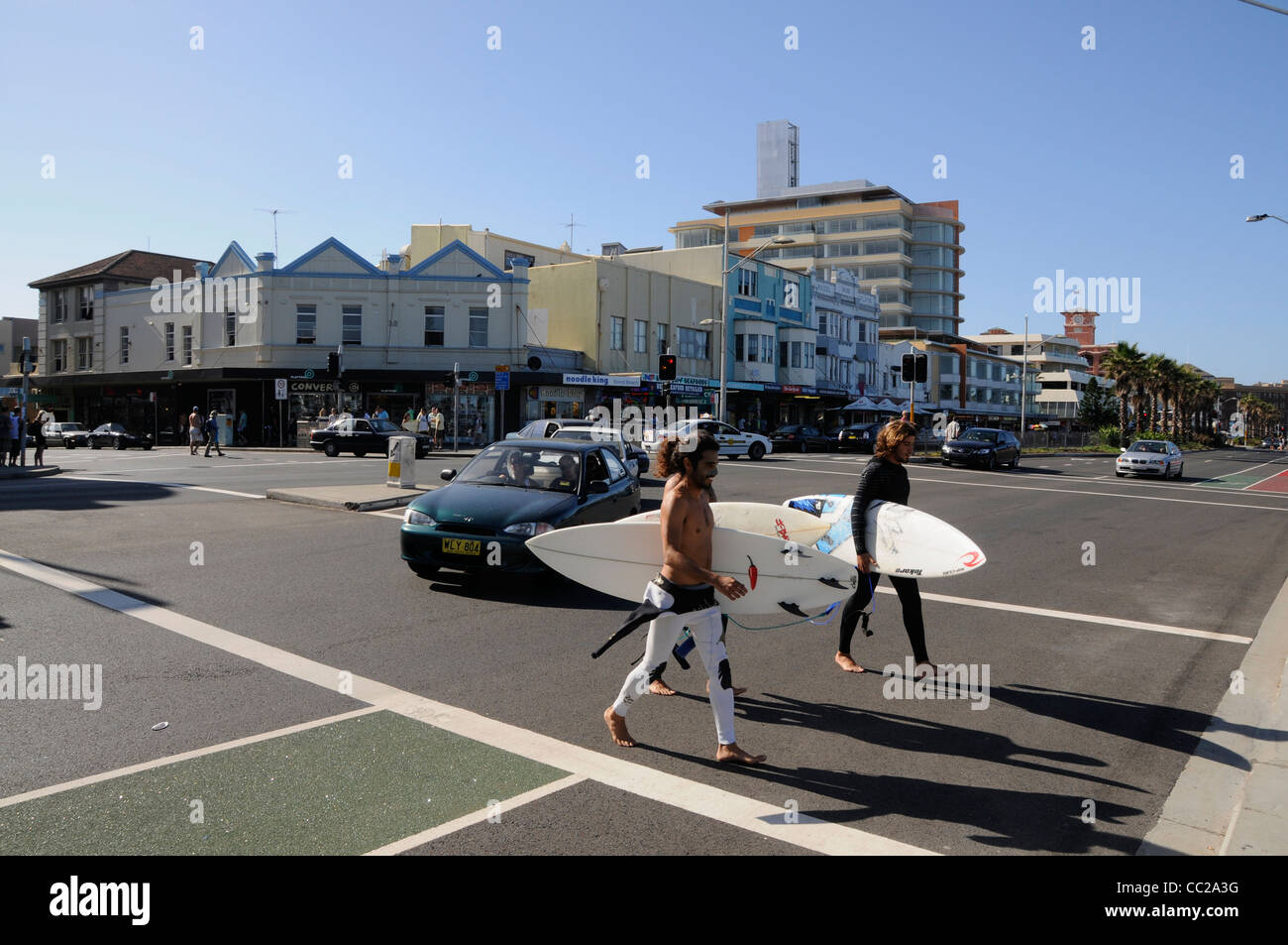 Trois jeunes hommes portant leurs planches de surf sur Campbell Parade jusqu'à la plage de Bondi Beach près de Sydney, en Australie Banque D'Images