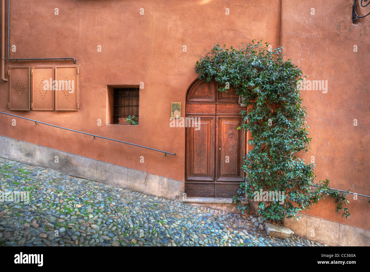 La porte en bois, petite fenêtre dans la chambre avec mur de couleur rouille sur la petite rue pavée de Saluzzo, Italie du nord. Banque D'Images