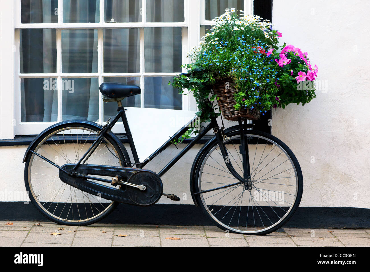 Photo d'un vieux vélo avec un panier rempli de fleurs et d'un panneau publicitaire vide dans le cadre. Banque D'Images