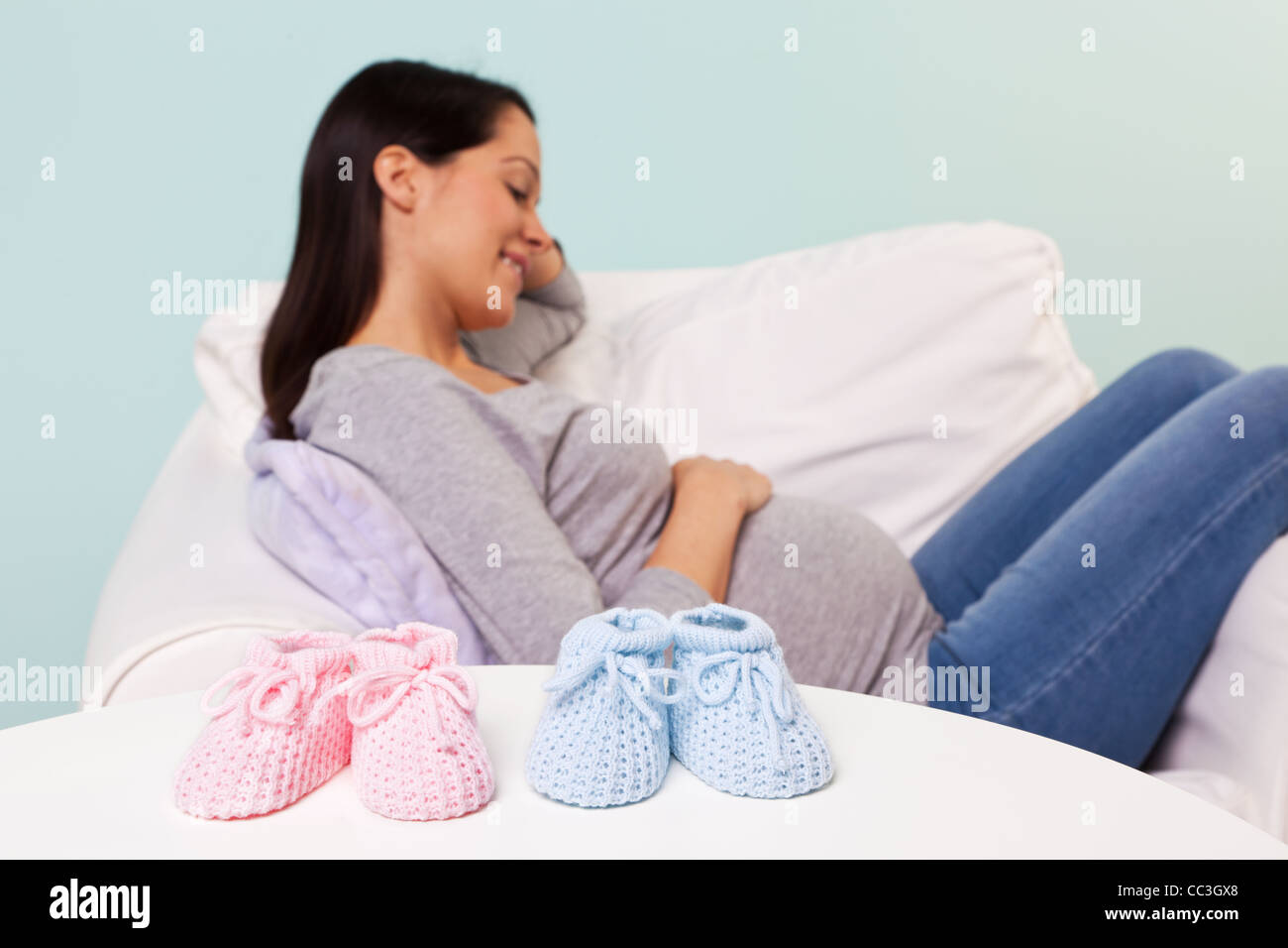 Photo d'une femme enceinte à la maison assis dans un fauteuil avec l'accent mis sur une paire de garçon et fille chaussons pour bébé tricotés Banque D'Images