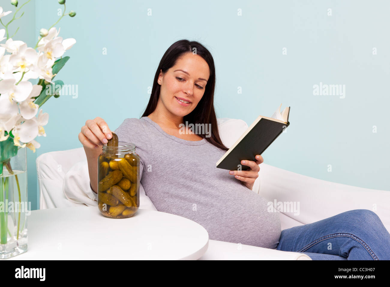 Photo d'une femme enceinte à la maison assis dans un fauteuil avec une envie de cornichons au vinaigre. Banque D'Images