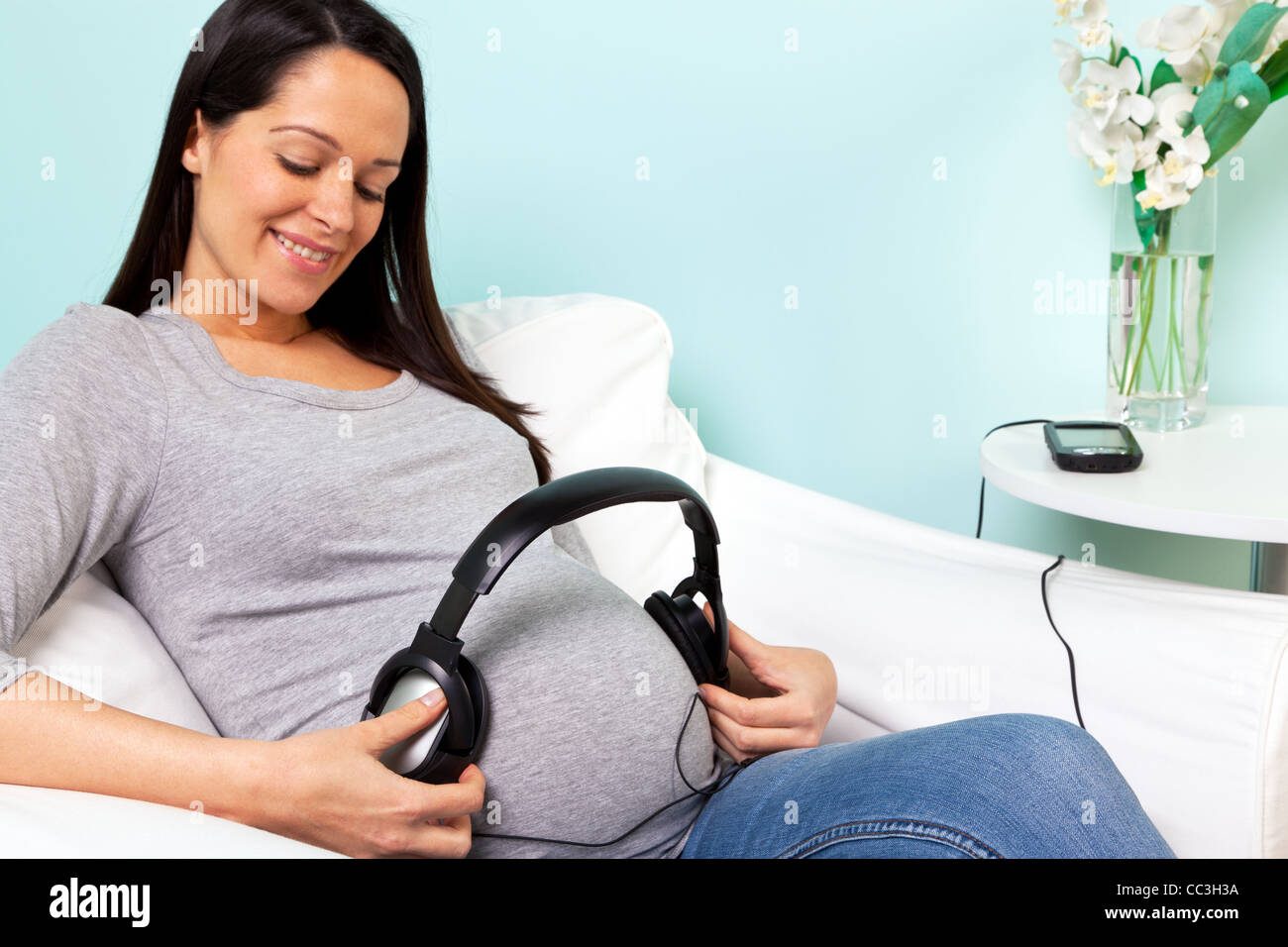 Photo d'une femme enceinte à la maison assis dans un fauteuil la lecture de la musique via des écouteurs à son bébé Banque D'Images