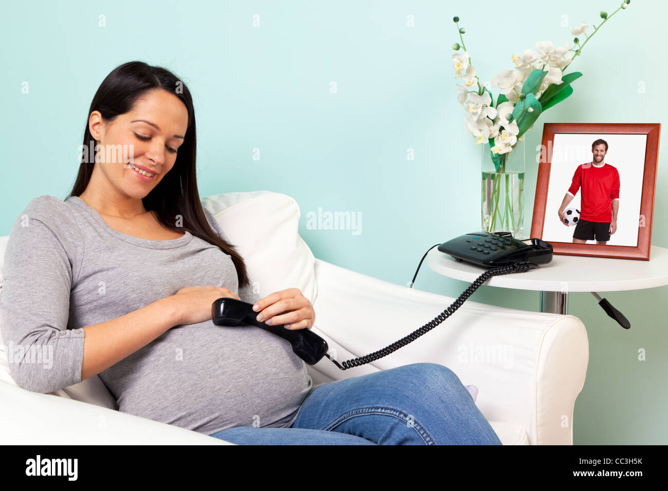 Photo d'une femme enceinte à la maison avec un combiné téléphonique sur son ventre, l'idée du père parler et écouter à l'enfant Banque D'Images