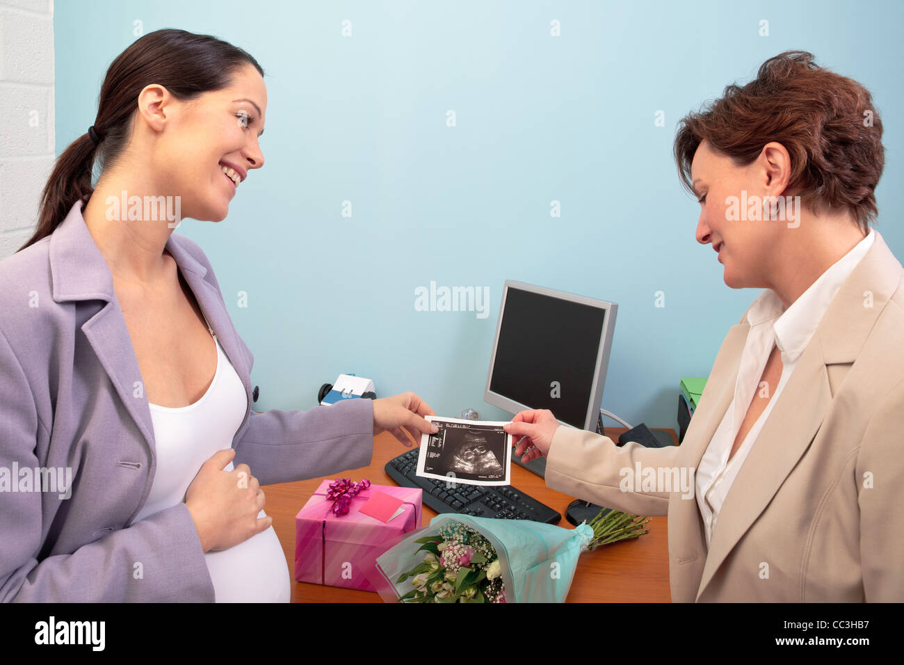Photo d'une des femmes enceintes au travail dans son bureau montrant son bébé échographie imprimer à un collègue Banque D'Images