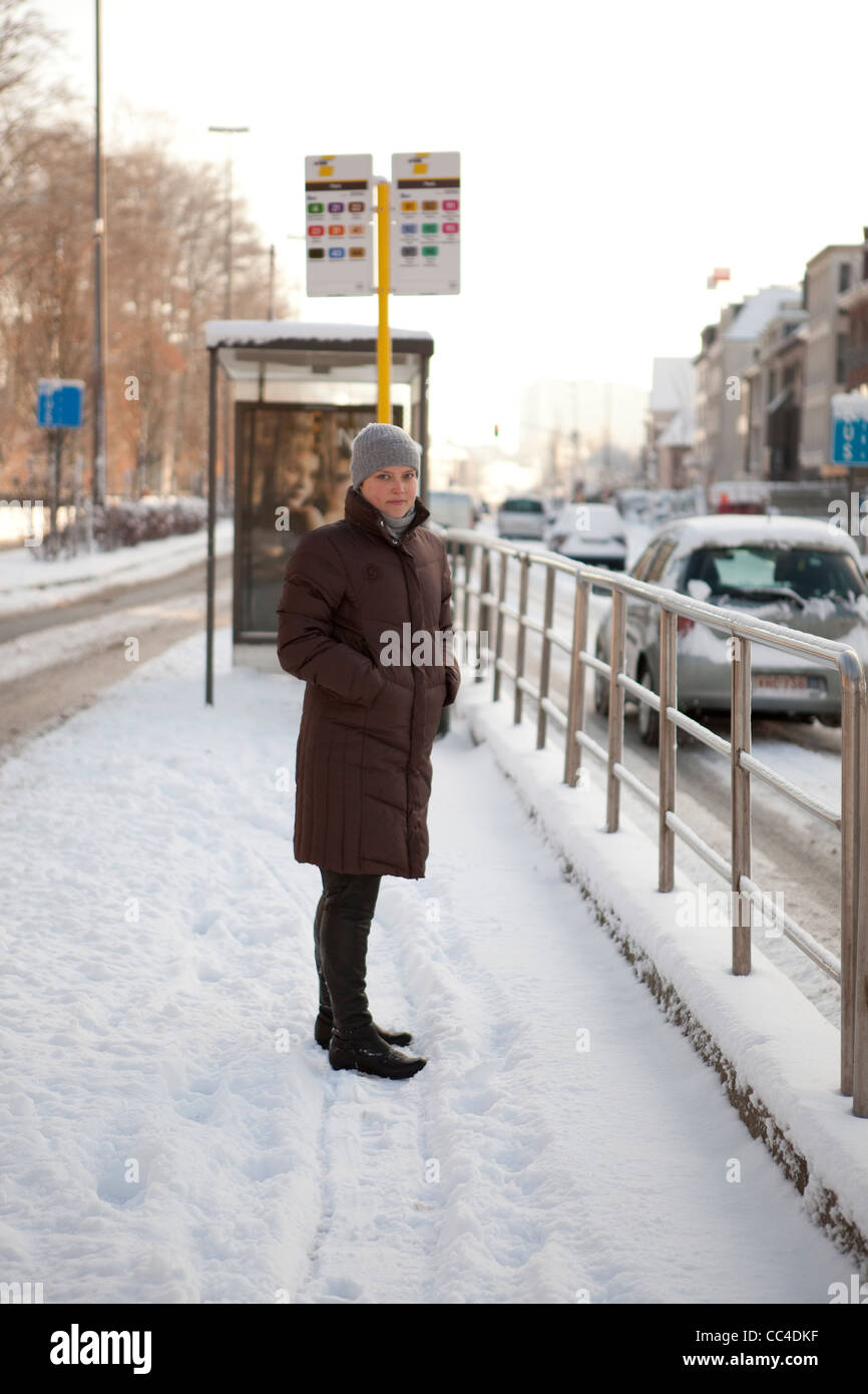 Une jeune femme est en attente de l'autobus à Sint-Niklaas, Belgique au cours d'une froide journée d'hiver avec la neige. Banque D'Images