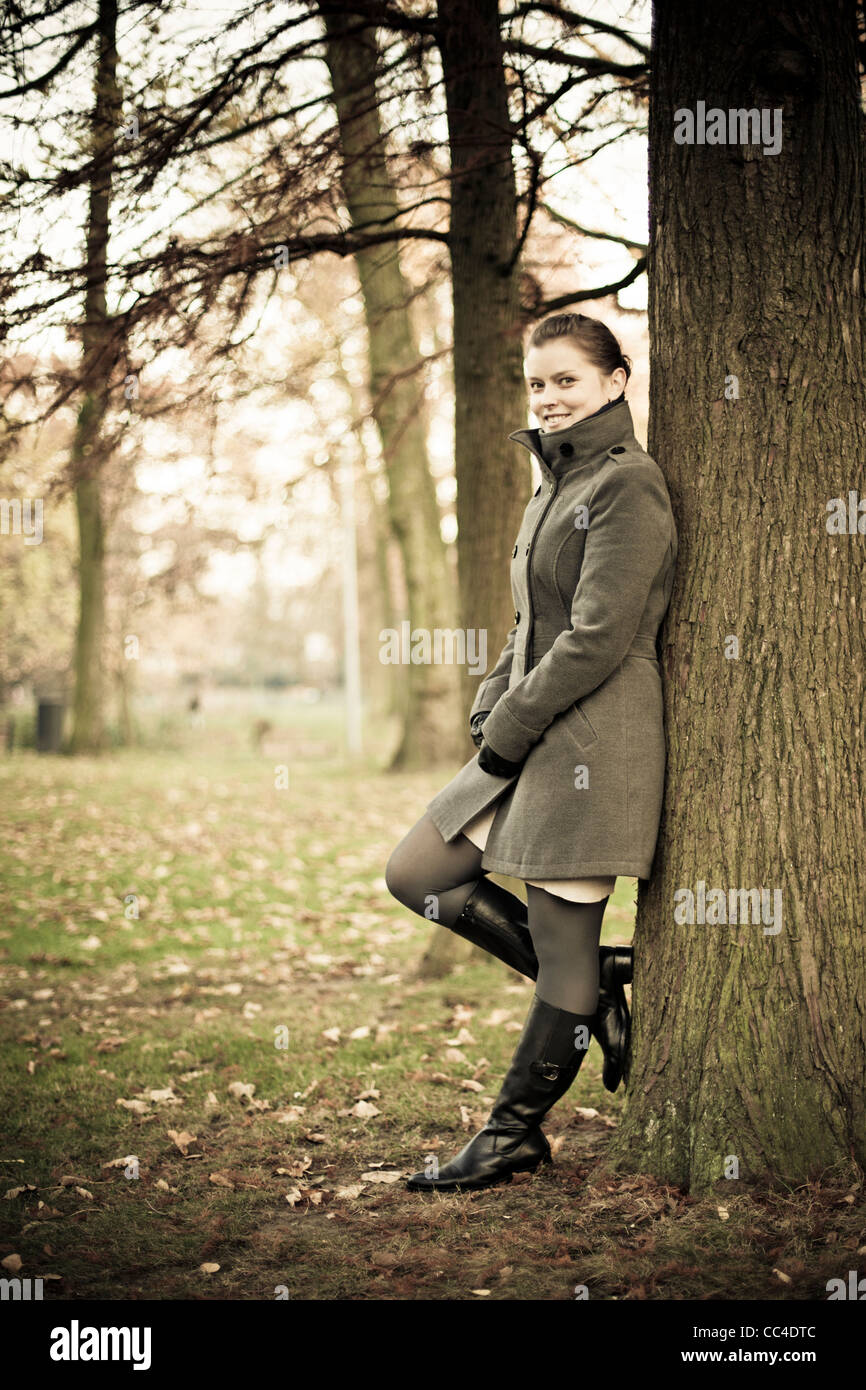Un modèle féminin avec un manteau et bottes de poser dans un parc avec des arbres dans une journée d'automne Banque D'Images