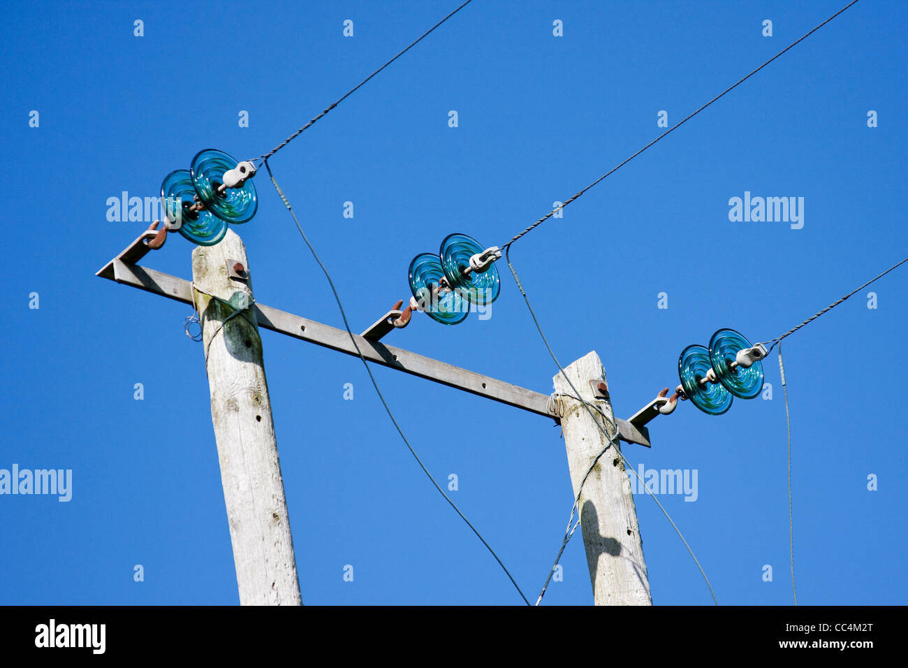 Des poteaux électriques avec fils et isolateurs en verre vert contre Ciel Bleu profond Banque D'Images