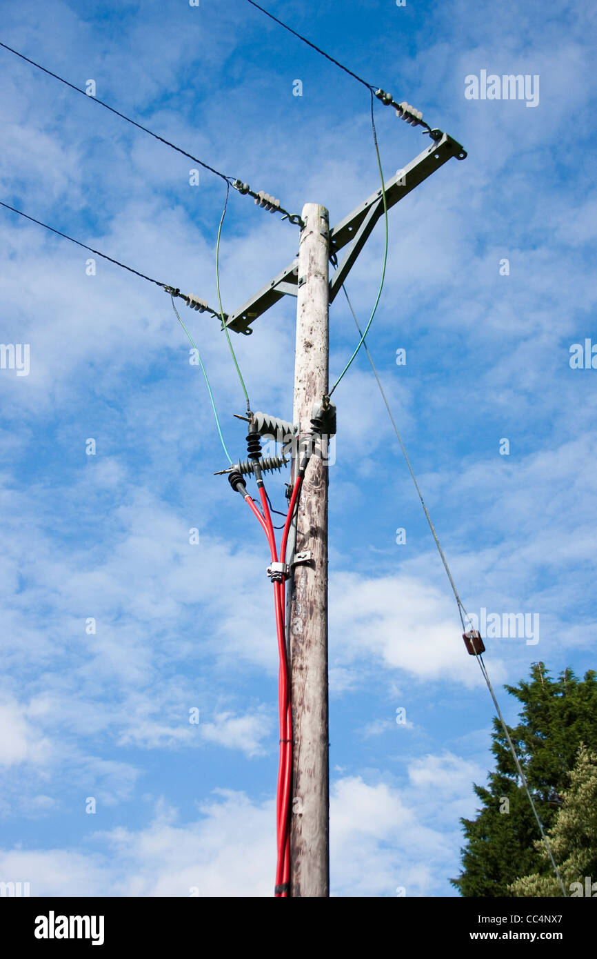 Pôle de l'électricité avec un rouge vif et des câbles aériens contre le ciel bleu Banque D'Images